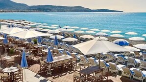A beachside restaurant with outdoor seating and umbrellas, overlooking a calm sea and distant hills. - 3-minute walk to the beach, private villa, garden, parking, tram (Nice)
