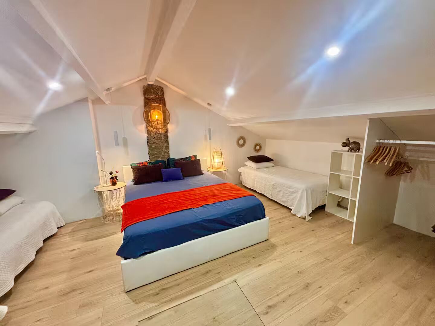 A bedroom with a large bed, a small bedside table, a wardrobe, and a stone wall with a light fixture.