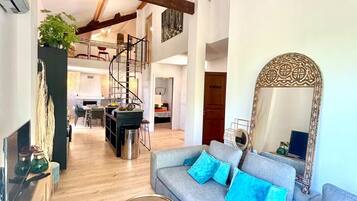A spacious living area with a large sofa, a coffee table, and a decorative mirror. A spiral staircase is visible in the background, leading to an upper level.