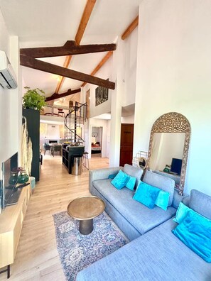 A spacious living area with a large sofa, a coffee table, and a decorative mirror. A spiral staircase is visible in the background, leading to an upper level. - 3-minute walk to the beach, private villa, garden, parking, tram (Nice)