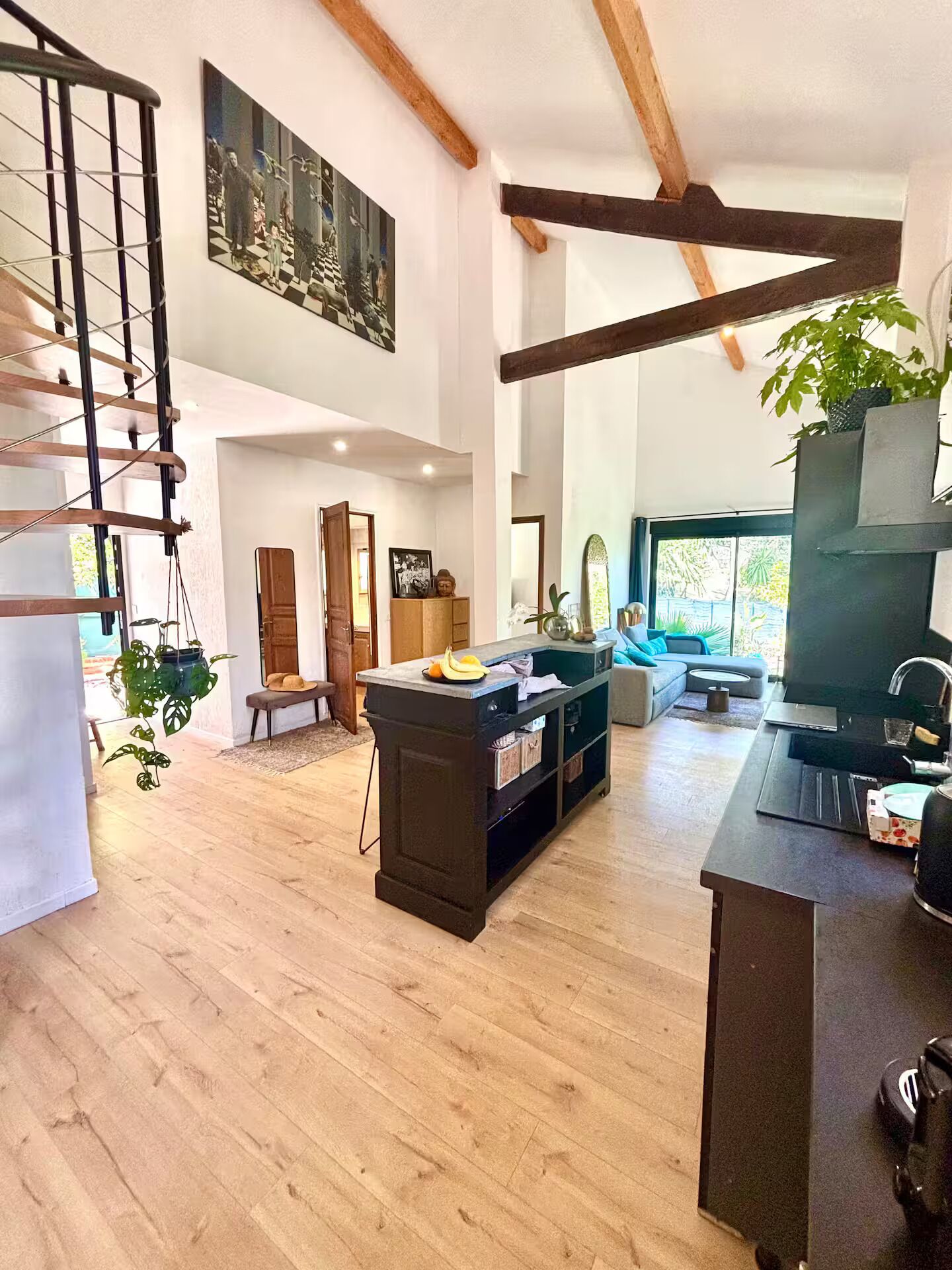 A spacious living area with a wooden staircase, a dining area with a central island, and a large window offering a view of the outdoors.