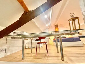 An attic bedroom with a glass ceiling, a wooden beam, a metal table, a red chair, a bed with a blue mattress, and a wall-mounted lantern. - 3-minute walk to the beach, private villa, garden, parking, tram (Nice)