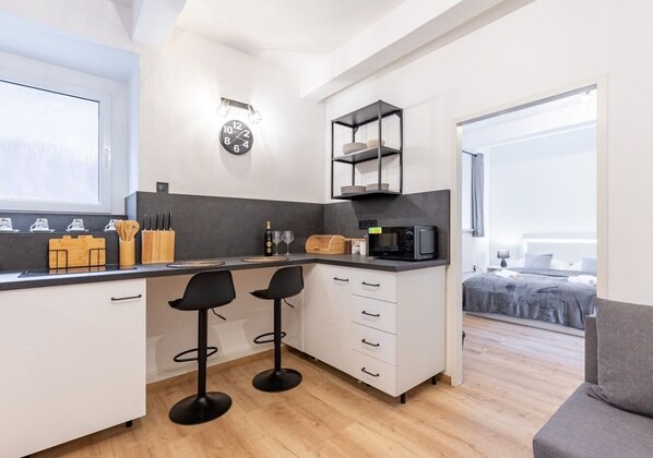 A modern kitchen with a microwave, bar stools, and a black shelf unit. - NO TAXI NEEDED, Central apartment w private courtyard (Bratislavský kraj)