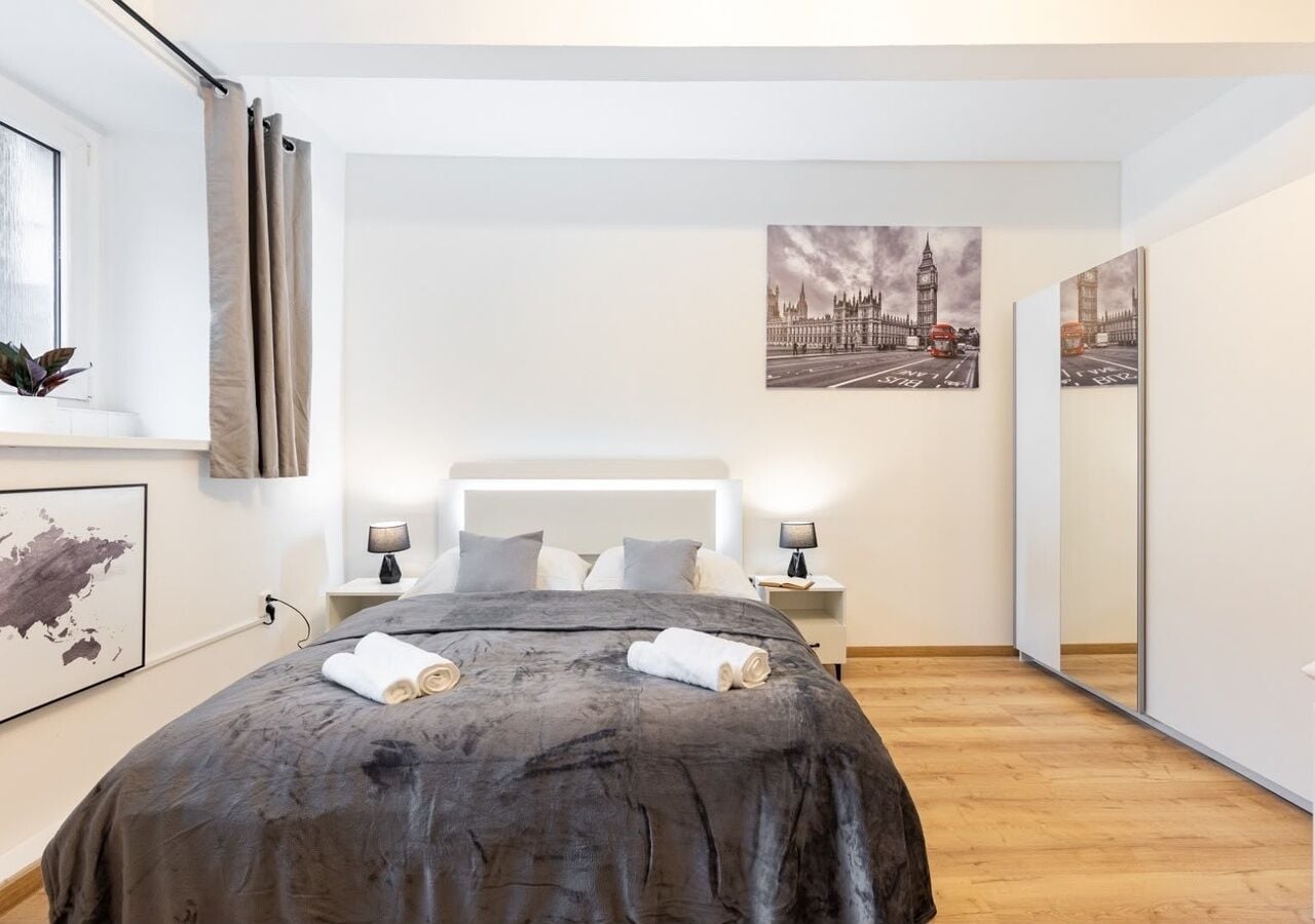 A modern bedroom with a large bed, two bedside tables with lamps, a large mirror, and artwork on the walls.