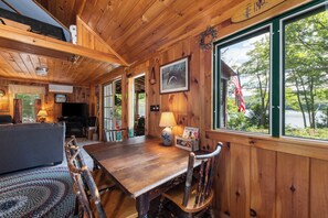 Un intérieur en bois comprenant une table à manger, des chaises, un téléviseur et une vue sur un lac.