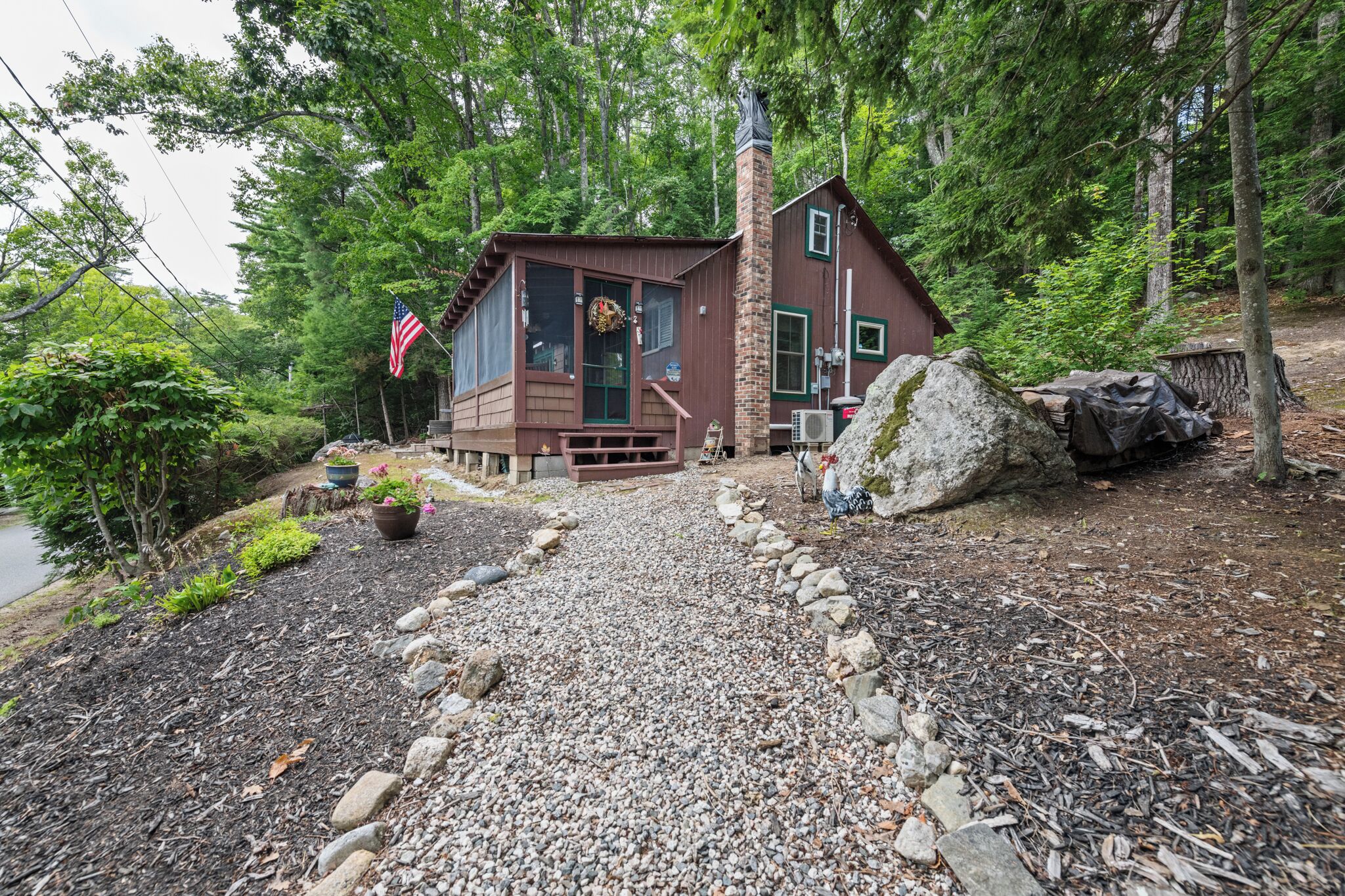 Eine Hütte mit Veranda, umgeben von einem Kiesweg und viel Grün.