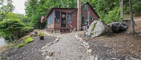 Eine Hütte mit Veranda, umgeben von einem Kiesweg und viel Grün.