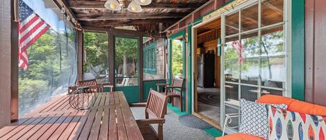 A covered outdoor seating area with wooden tables and chairs, a flag, and a view of the outdoors.