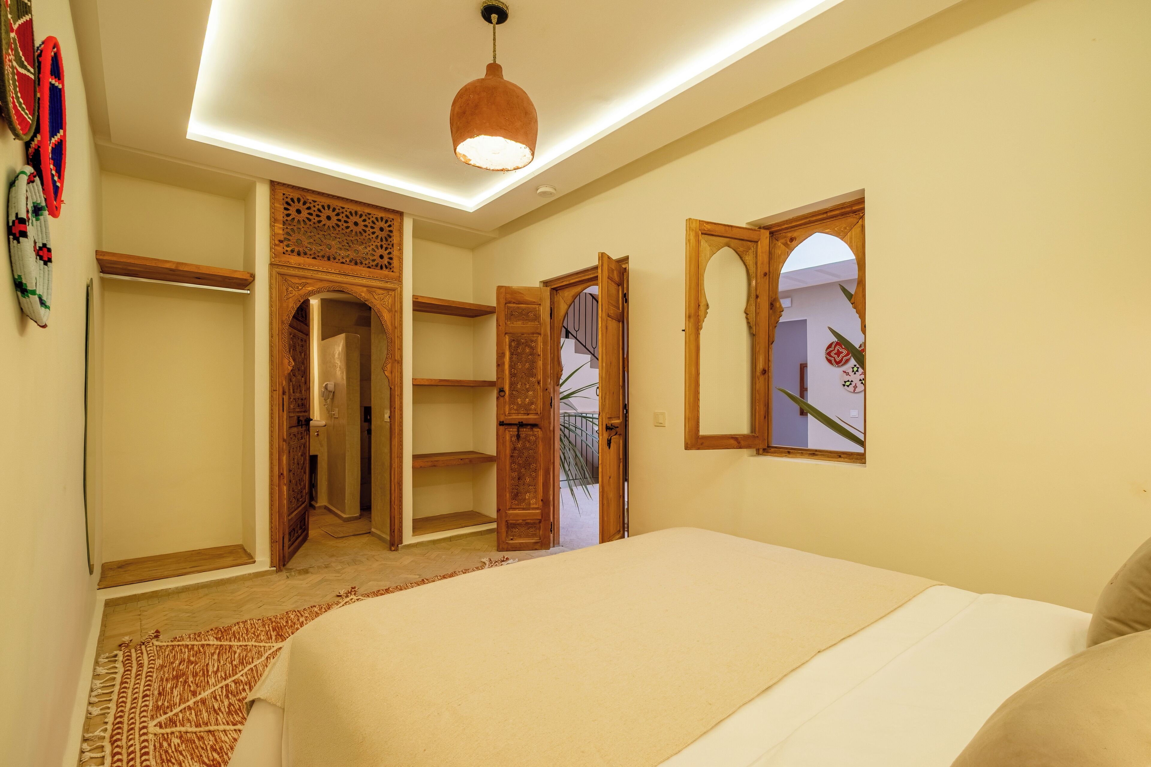A bedroom with a bed, a wooden wardrobe, a mirror, and a door leading to a staircase.
