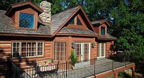 A log cabin with a porch, a dining table, and a black metal fence. - Celebrate Labor Day weekend in the Missouri Ozarks in this cabin for 6 guests. (Ridgedale)