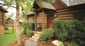 A log cabin with a stone pathway leading to the entrance, surrounded by greenery and a stack of firewood. - Celebrate Labor Day weekend in the Missouri Ozarks in this cabin for 6 guests. (Ridgedale)