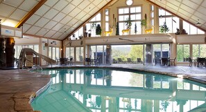 An indoor swimming pool with a slide, surrounded by tables and chairs, and large windows offering views of the outdoors. - Celebrate Labor Day weekend in the Missouri Ozarks in this cabin for 6 guests. (Ridgedale)