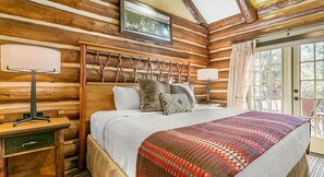A log cabin bedroom with a bed, bedside lamps, and a window with curtains. - Celebrate Labor Day weekend in the Missouri Ozarks in this cabin for 6 guests. (Ridgedale)