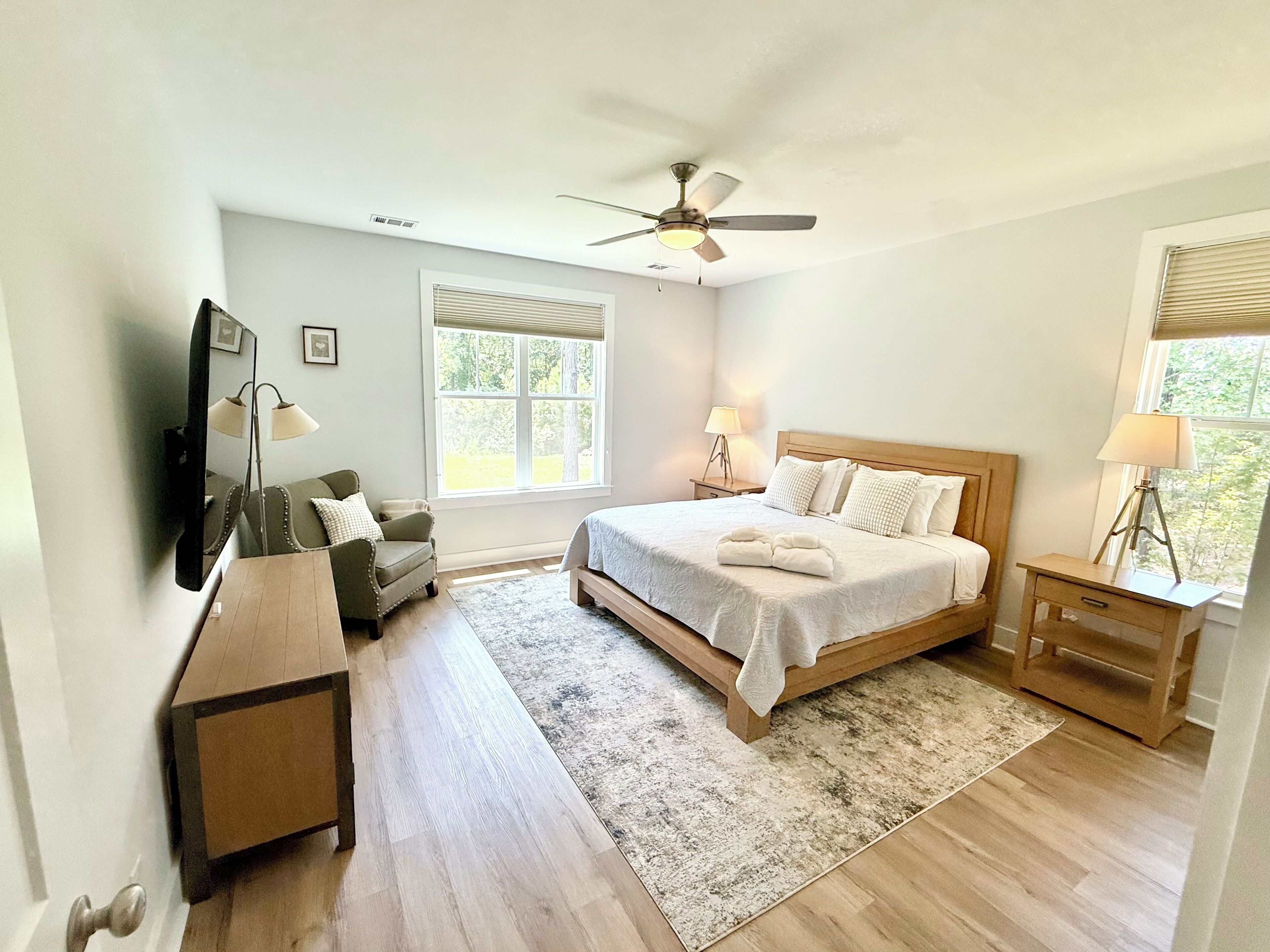 Quarto com cama, mesas de cabeceira, uma cadeira, escrivaninha, ventoinha no teto e janela.