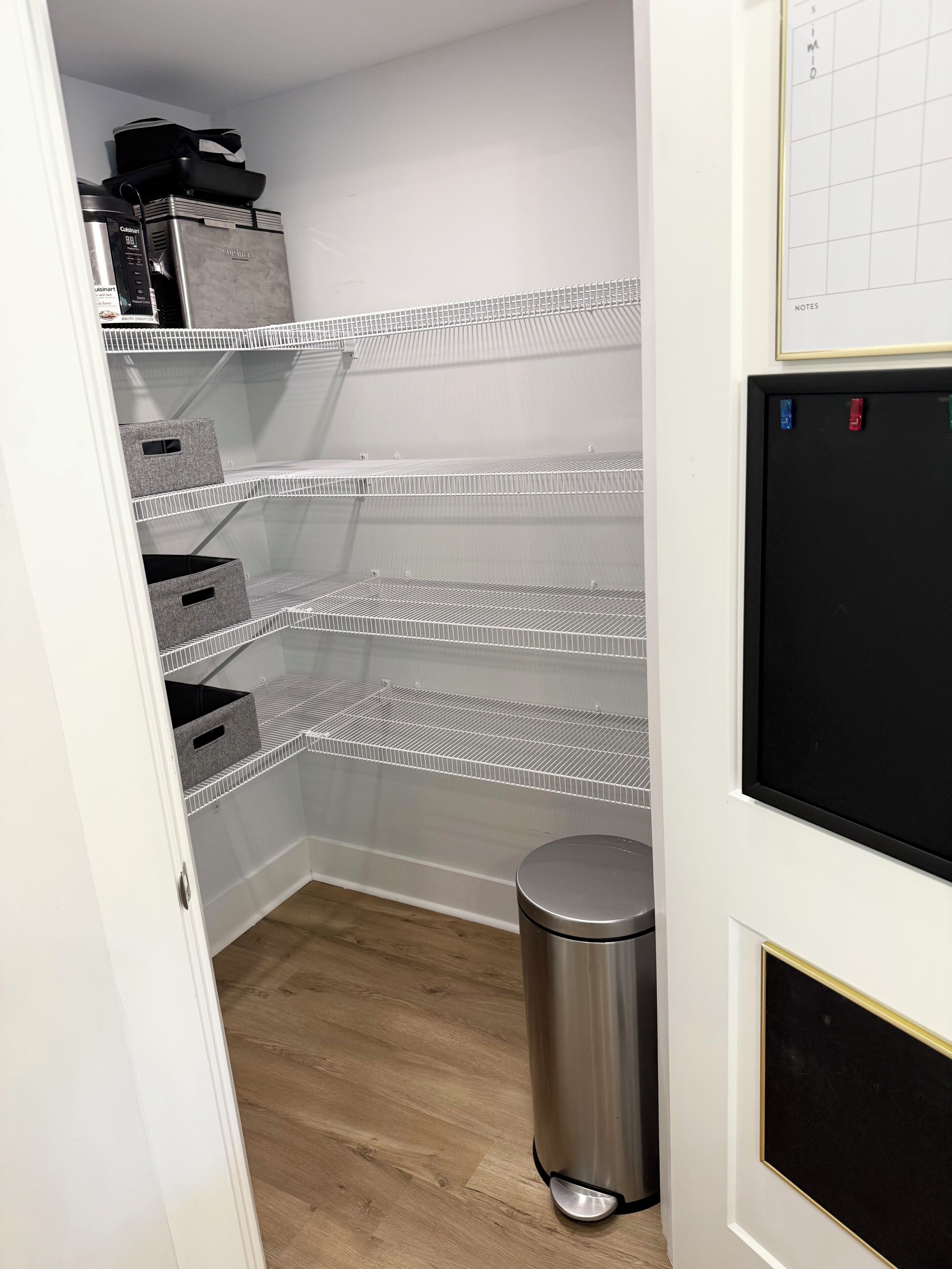 Uma área de armazenamento com prateleiras de metal, um cesto de lixo e um quadro negro com anotações.