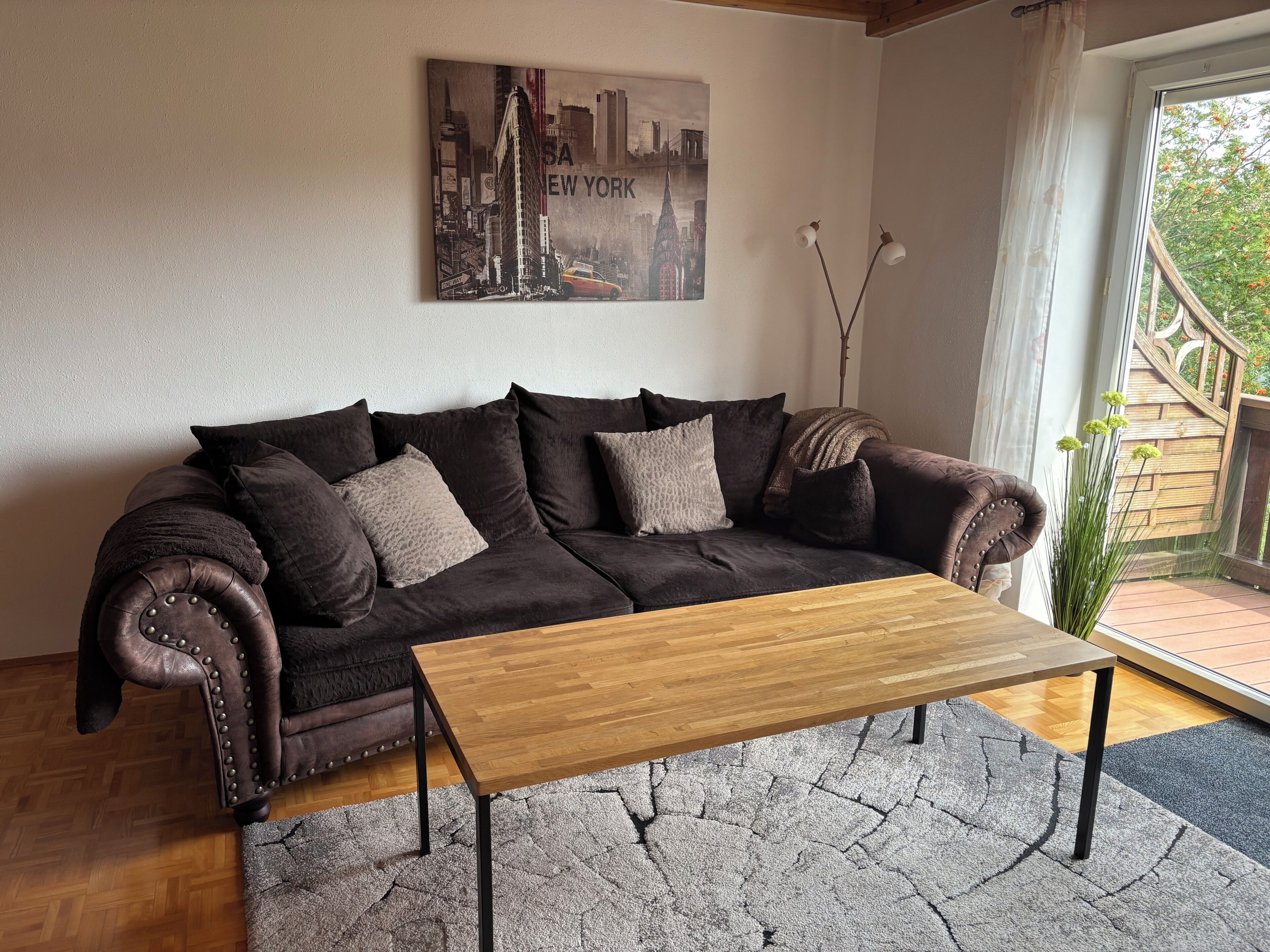 A brown leather sofa with cushions, a wooden coffee table, and a cityscape painting on the wall.