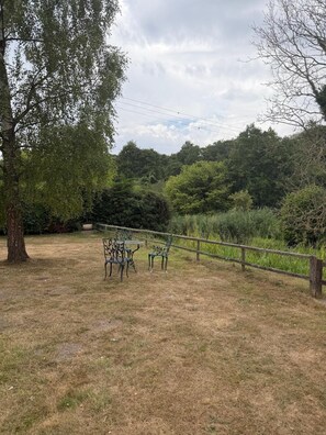 A grassy outdoor area with a wooden fence, metal chairs, and a tree.