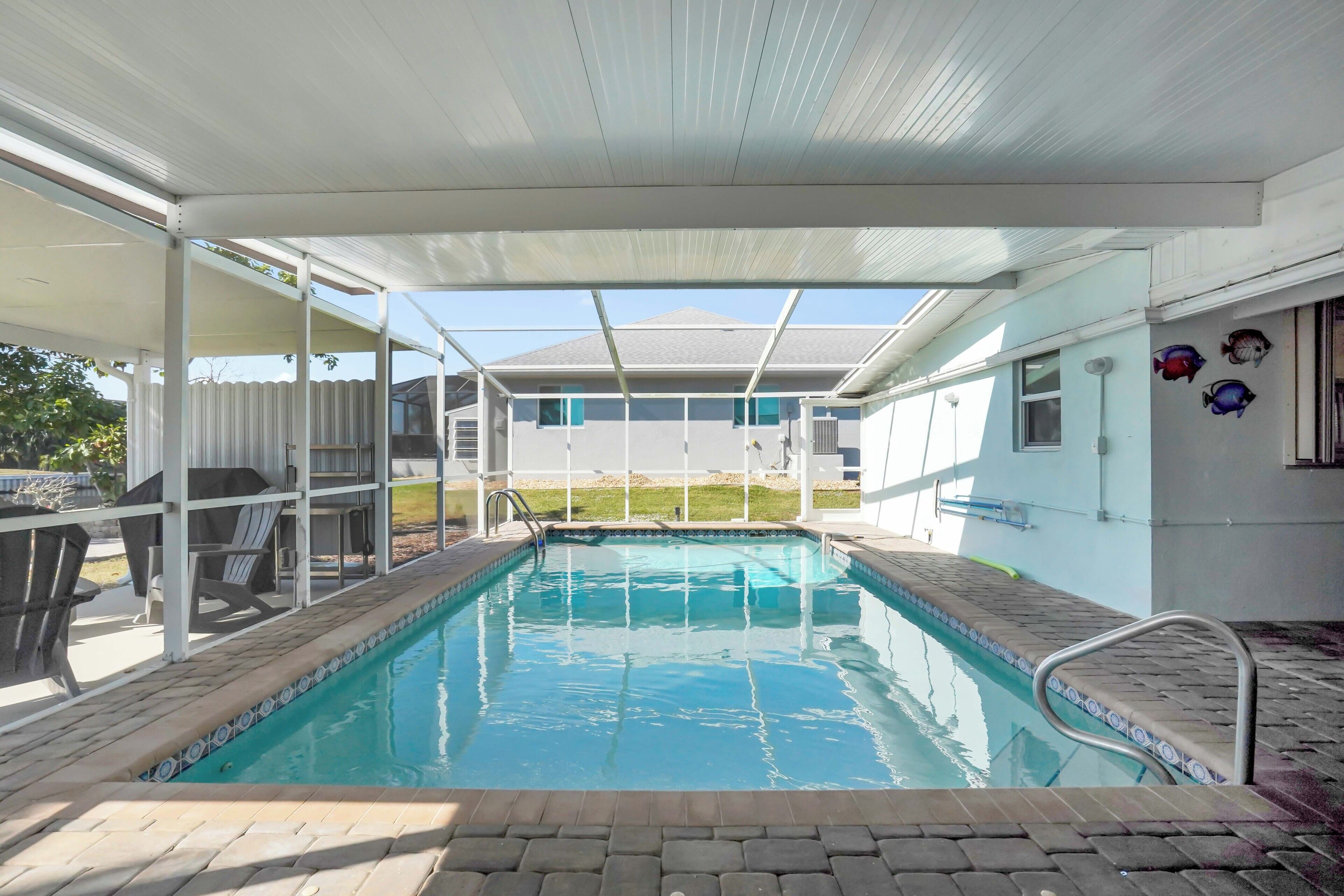 A swimming pool with a covered area, clear blue water, and a view of a house in the background.