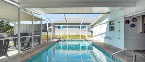 A swimming pool with a covered area, clear blue water, and a view of a house in the background.