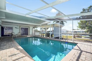 A pool area with a clear view of the sky, a covered seating area, and a poolside chair. - Harbor Haven Waterfront Oasis + Heated Pool (Port Charlotte)