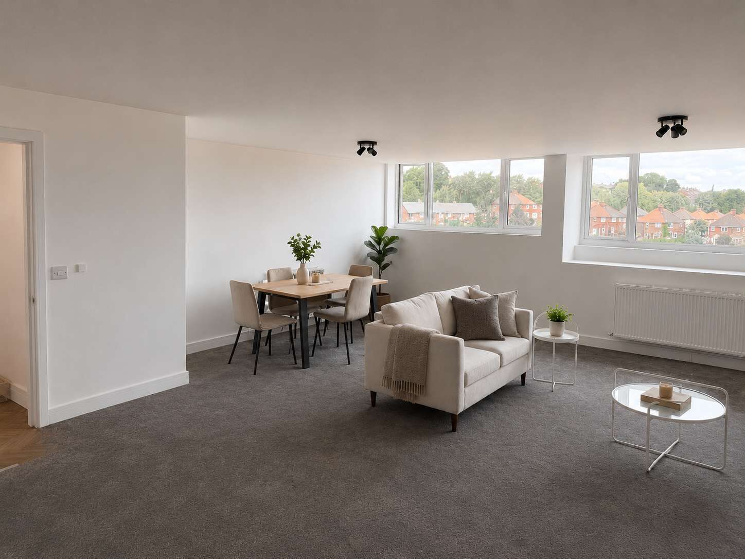 Un salon moderne comprenant un canapé, une table à manger avec des chaises, une petite table ronde ornée d’une plante, et une vue sur l’extérieur grâce à de grandes fenêtres.