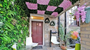 A courtyard with a red door, white and green chairs, and a variety of plants. - RM4 - Perfect 1-bedroom, Shower inside room with free onsite parking. (Aberdeen)