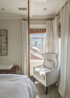 Une chambre à coucher comprenant un lit, une chaise, une fenêtre avec des rideaux et une œuvre d’art accrochée au mur.