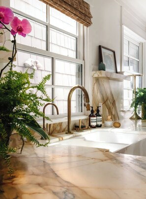 Un bagno con un lavandino in marmo, un rubinetto dorato e un'ampia finestra con persiane.