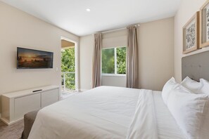 Ein Schlafzimmer mit Bett, Nachttisch, einem an der Wand montierten Fernseher und einem Fenster mit Vorhängen.
