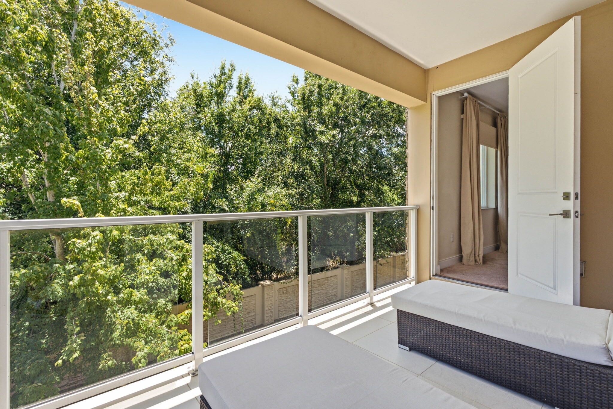 A balcony with a white railing, a white bench, and a door leading to an interior space.