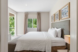 Ein Schlafzimmer mit einem großen Bett, einem Fenster mit Vorhängen und gerahmten Kunstwerken an der Wand.