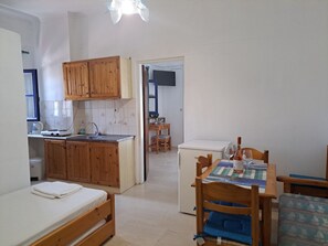A compact kitchen with wooden cabinets, a dining table with chairs, and a small refrigerator. - Marvelous 1-bedroom apartment with AC in Αγια Πελαγια (ΑΓΙΑ ΠΕΛΑΓΙΑ)