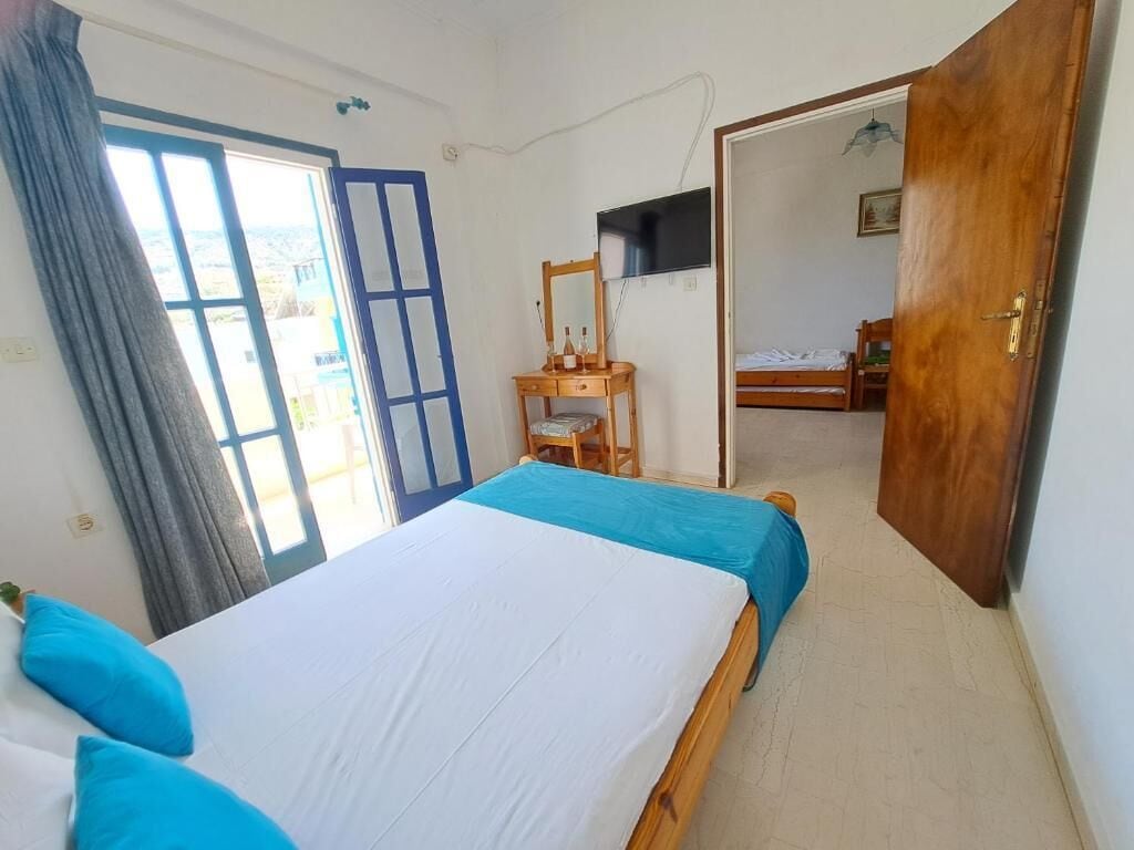 Un dormitorio con cama, escritorio, televisor y una puerta que da a otra habitación.