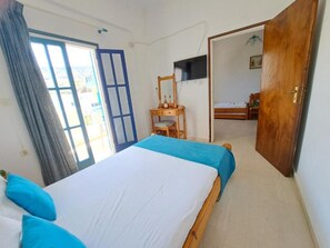 A bedroom with a bed, a desk, a television, and a door leading to another room. - Marvelous 1-bedroom apartment with AC in Αγια Πελαγια (ΑΓΙΑ ΠΕΛΑΓΙΑ)