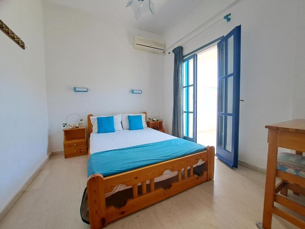 Un dormitorio con una cama de madera, una mesita de noche, una silla y una ventana con cortinas.