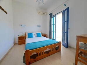 A bedroom with a wooden bed, a bedside table, a chair, and a window with curtains. - Marvelous 1-bedroom apartment with AC in Αγια Πελαγια (ΑΓΙΑ ΠΕΛΑΓΙΑ)