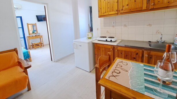 Uma cozinha compacta com armários de madeira, uma geladeira branca e um espaço de refeições com uma mesa posta para dois.