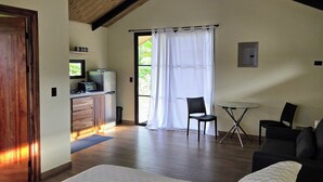 Een slaapkamer met een groot bed, een houten plafond, een kleine kitchenette en een eethoek met stoelen.