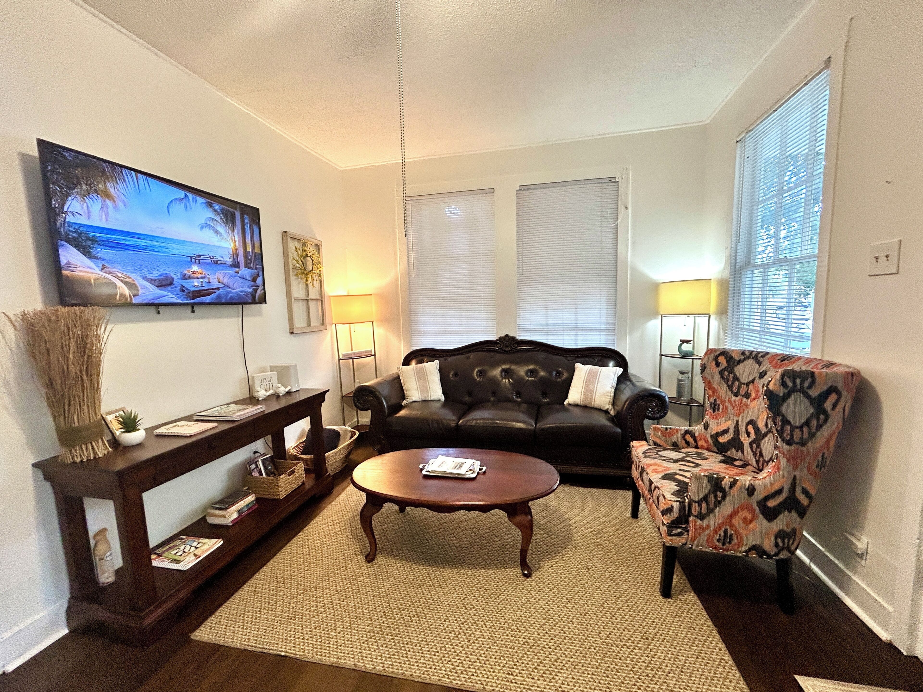 A living room with a dark leather sofa, a patterned armchair, a coffee table, and a flat-screen TV mounted on the wall.