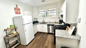Una cocina con gabinetes blancos, un refrigerador de acero inoxidable, un microondas, un lavavajillas y una estufa a gas.