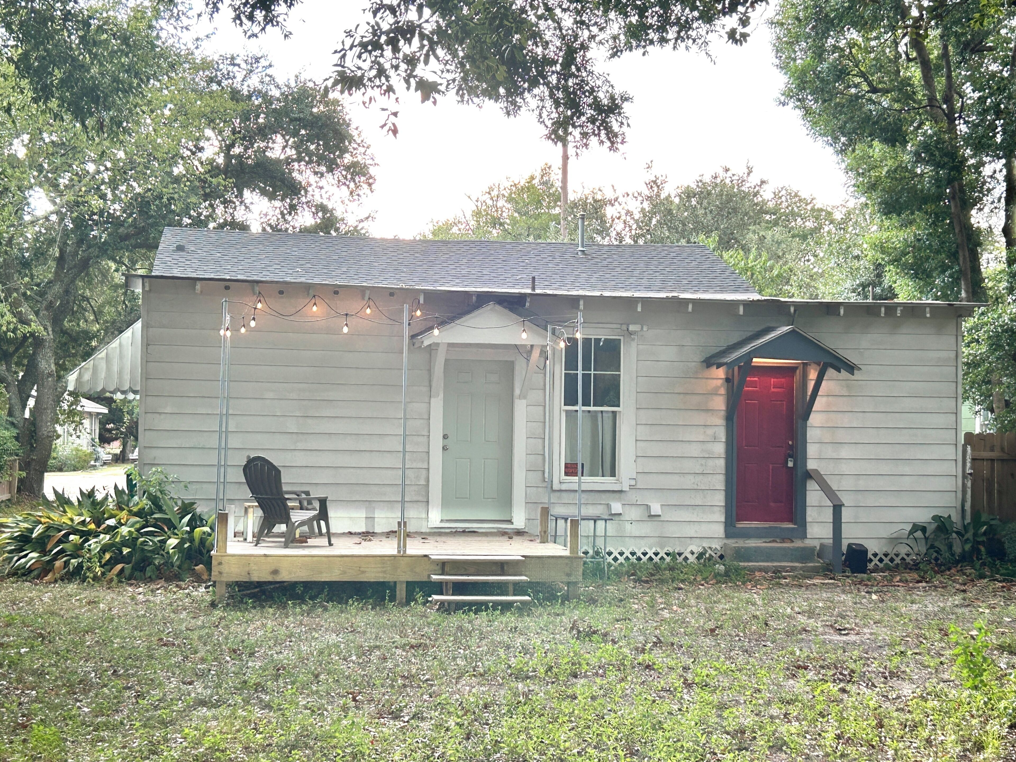 A small house with a porch, a red door, and string lights.