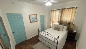 Un dormitorio con cama, ventilador de techo, mesita de noche y una puerta.