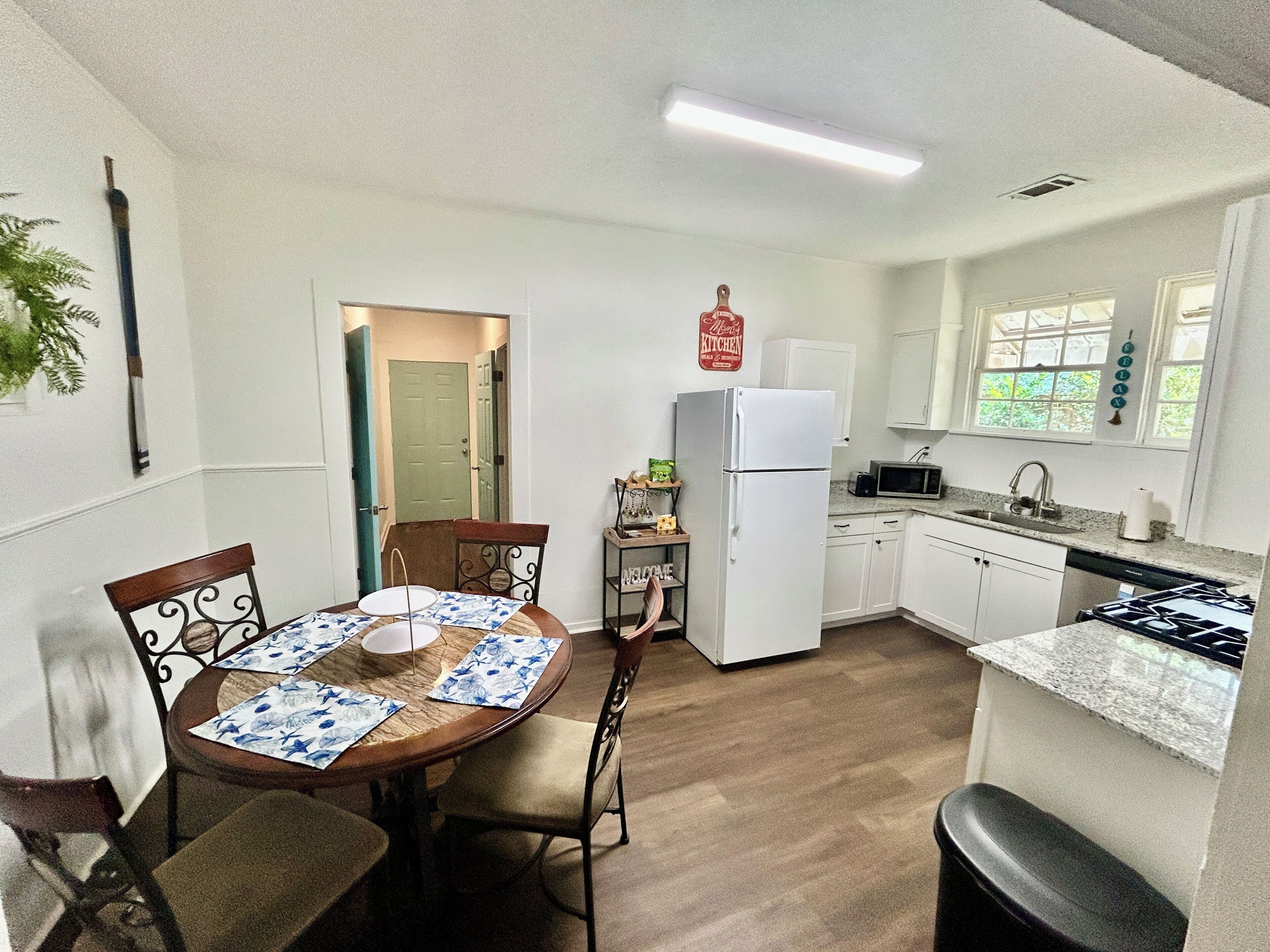 A compact kitchen with a dining area, white cabinets, a refrigerator, a microwave, and a stove.