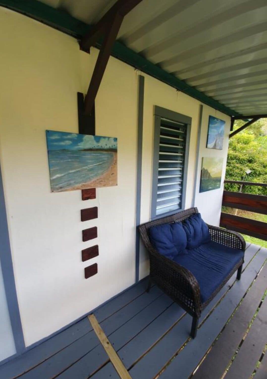 A covered porch with a wicker sofa and a wall-mounted artwork.