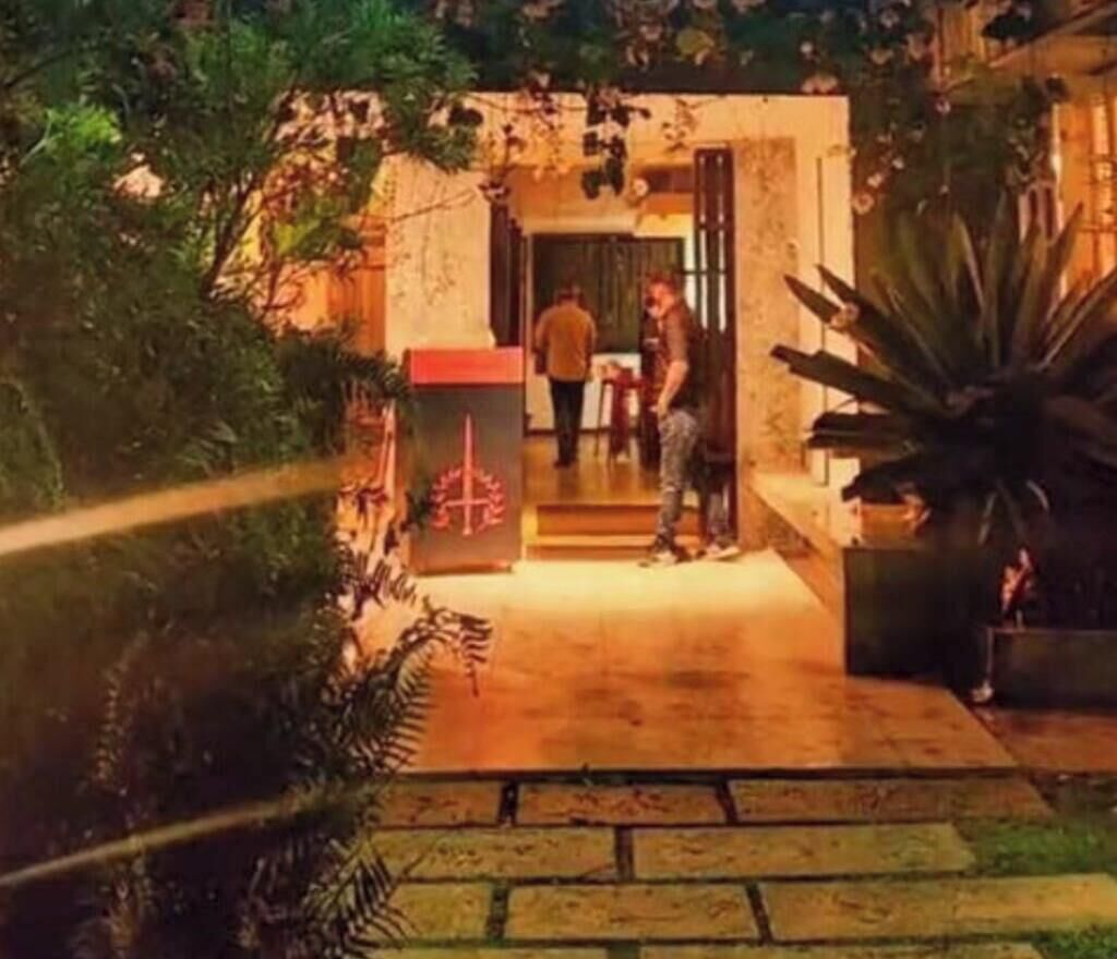 Entrada de hotel con un camino de piedra que lleva a una puerta, rodeada de vegetación.