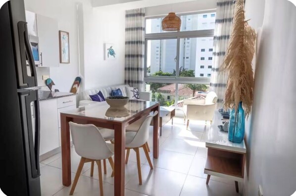 A modern kitchen with a dining area, large windows, and a view of buildings outside. - Excentric at Juan Dolio Beach (Juan Dolio)