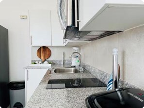 A compact kitchen with a granite countertop, stainless steel sink, and a built-in oven. - Excentric at Juan Dolio Beach (Juan Dolio)