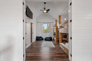 A narrow hallway with wooden flooring, a ceiling fan, and bunk beds on one side. - Hot Tub, Fire Pit, Ping Pong, Near Beavers Bend (Broken Bow)