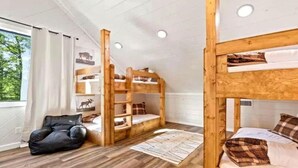 Ett rum med våningssängar, en svart stol och ett fönster med gardiner.