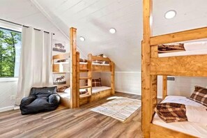 Ein Zimmer mit Etagenbetten, einem schwarzen Sessel und einem fenster mit Vorhängen.